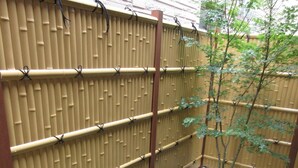 A bamboo fence with a small tree and shrubbery in a gravel area. - Kyoto Oyado ZEN (Kyoto)