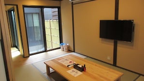 A room with a wooden table, a television mounted on the wall, and a sliding door leading to an outdoor area. - Kyoto Oyado ZEN (Kyoto)