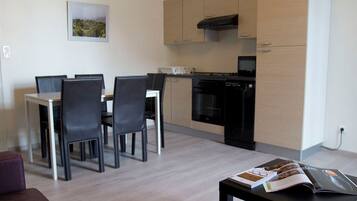 A modern living room with a sofa, a dining area with chairs and a table, and a kitchen with cabinets and appliances.