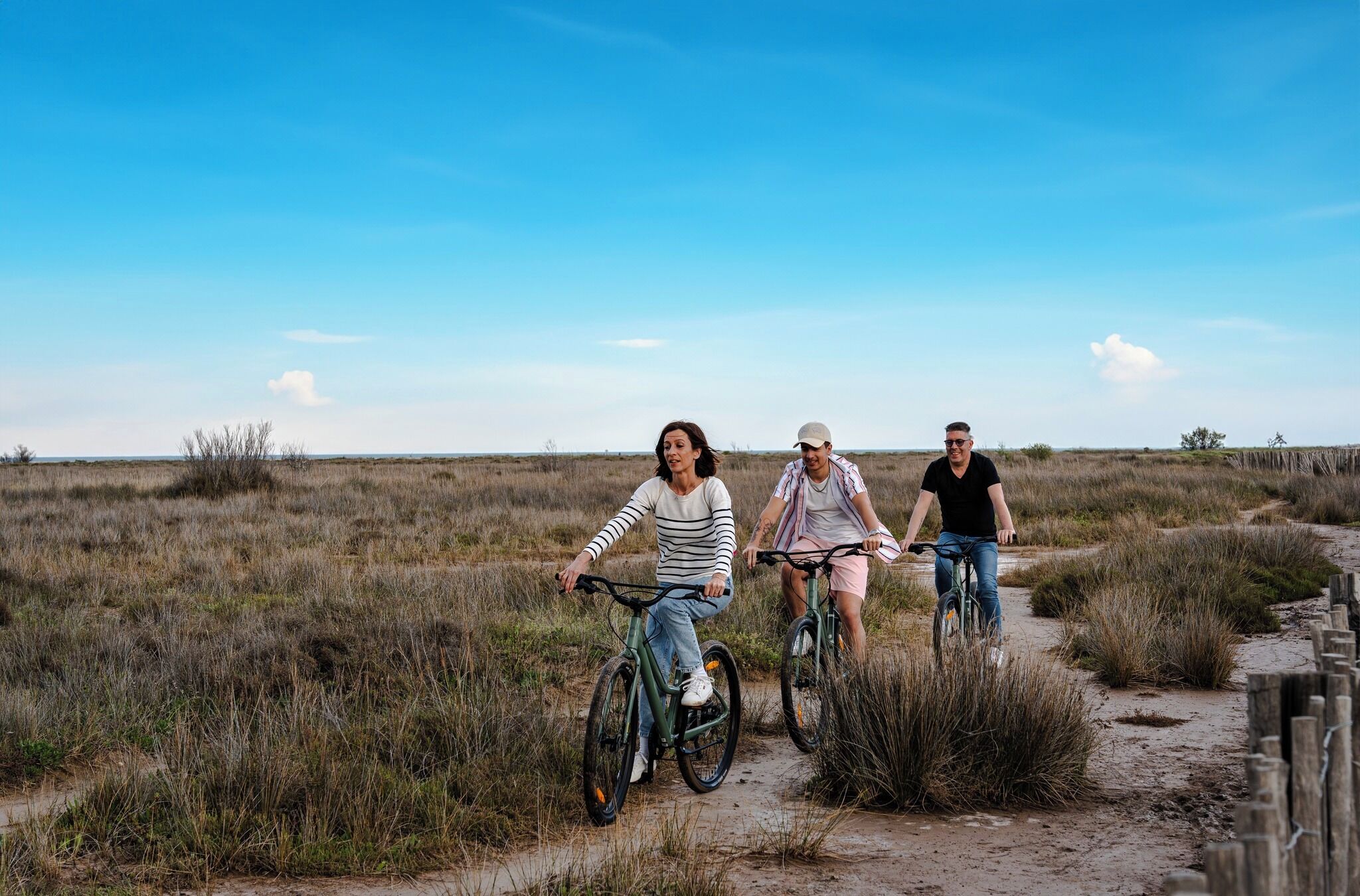 Three people riding bicycles on a dirt path in a natural landscape.