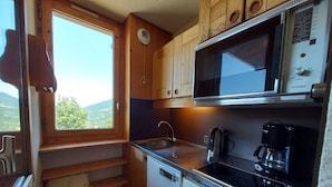Een kleine keuken met houten kastjes, een magnetron, een koffiezetapparaat en een vaatwasser.