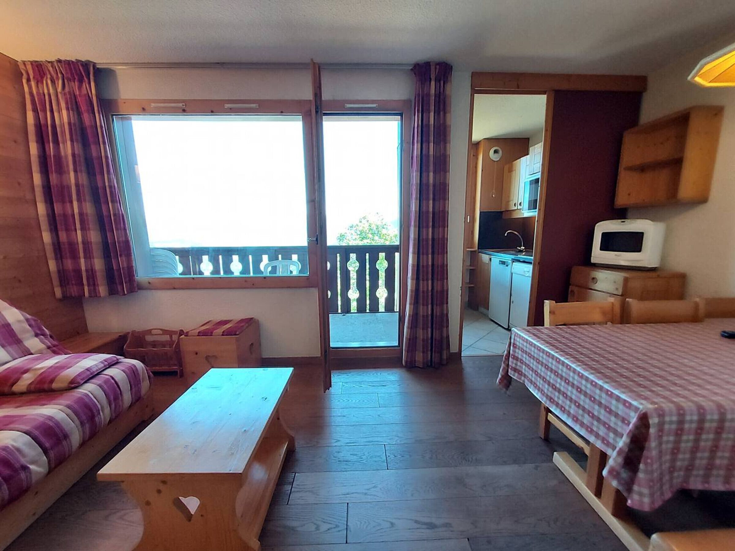 Una stanza accogliente con un divano, un tavolo di legno, un letto con copriletto a quadretti e un angolo cottura sullo sfondo.
