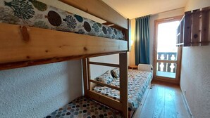 Een slaapkamer met een stapelbed, een bed met een patroon, een raam met gordijnen en een houten leuning.