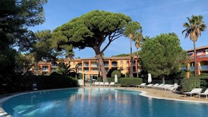 Une piscine entourée d’arbres, avec des chaises longues et un bâtiment doté de balcons.
