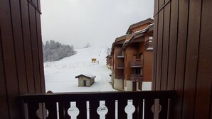 Un bâtiment en bois doté de balcons, une pente enneigée et une petite cabane visible au loin.