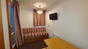 Une petite pièce avec un banc en bois, un canapé, un téléviseur fixé au mur et une porte avec des rideaux.