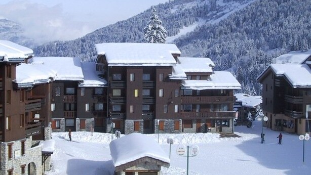 Une station de ski enneigée comprenant plusieurs bâtiments, notamment un bâtiment principal doté d’une façade en pierre et un autre bâtiment en bois avec un toit en pente.