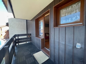 A wooden balcony with a bench, a door leading to an interior room, and a window with a decorative pattern.
