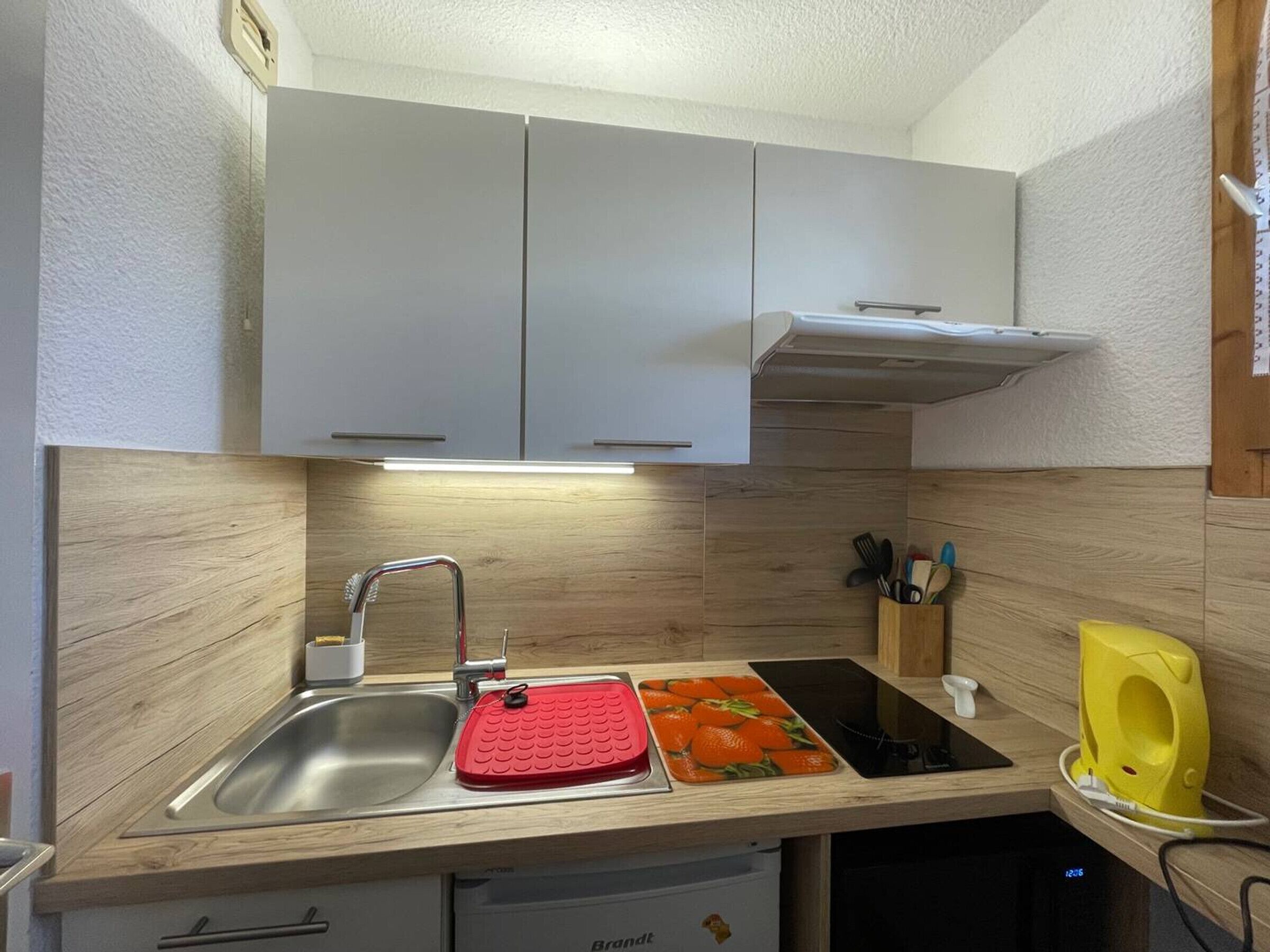 Una cocina con un lavamanos de acero inoxidable, una tabla de cortar roja y una cocina vitrocerámica negra.