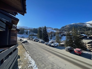 A road with parked cars, a building with a sloped roof, and snow-covered mountains in the background.