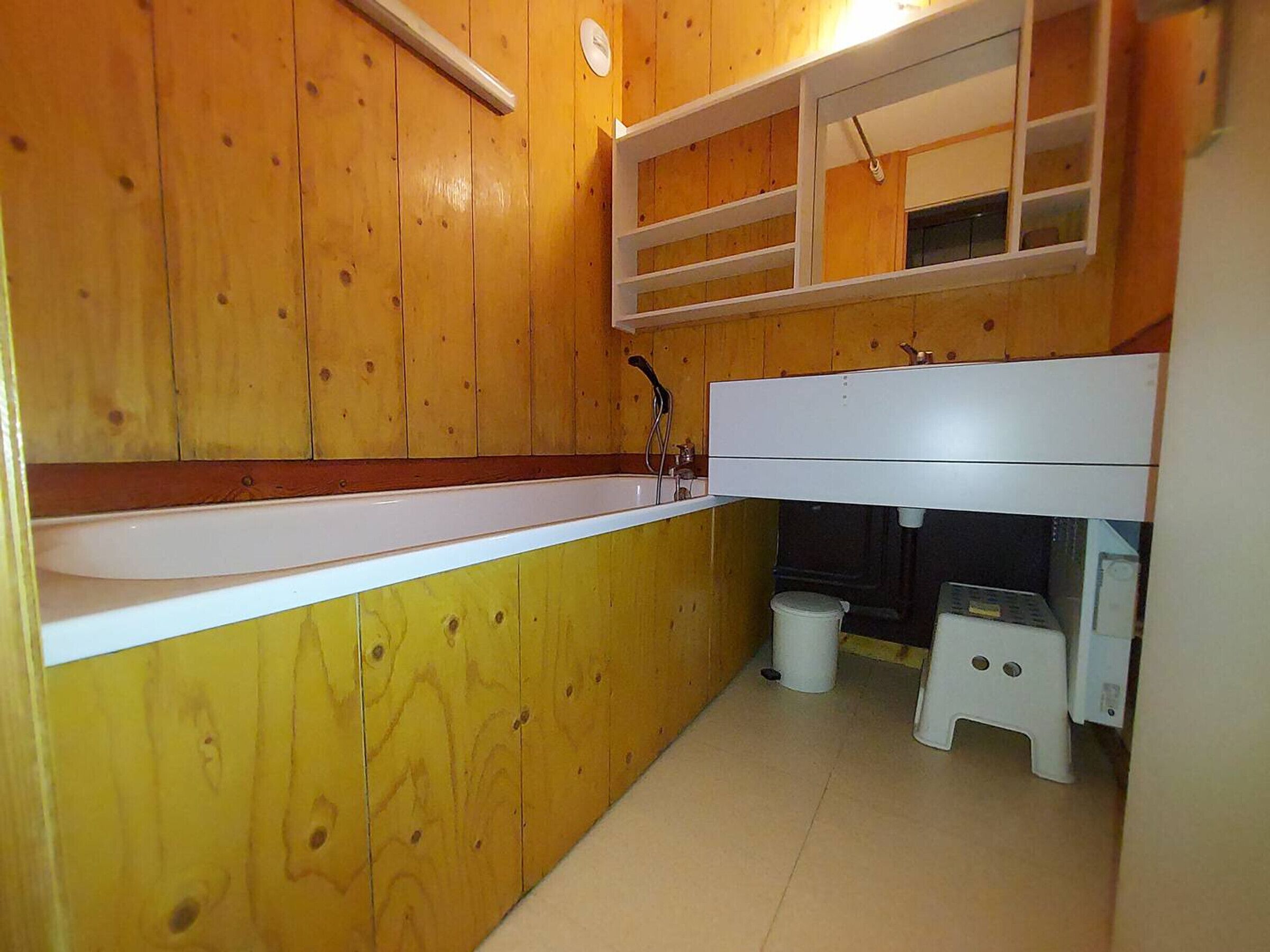 A small, compact bathroom with wooden walls, a white sink, and a mirror above it.