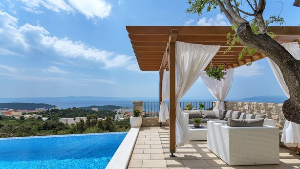 Zona de piscina privada con un pérgola, mobiliario de mimbre blanco y vistas al paisaje.