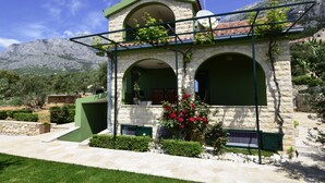 Un edificio de piedra con techo verde y ventanas arqueadas, rodeado de vegetación y montañas.