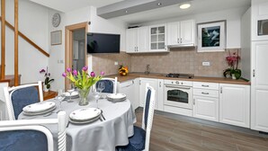 Una cocina moderna con armarios blancos, un comedor con una mesa para dos personas y una escalera que sube a otro nivel.