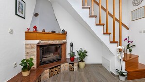 Una sala de estar moderna con chimenea, escalera de madera y plantas en macetas.