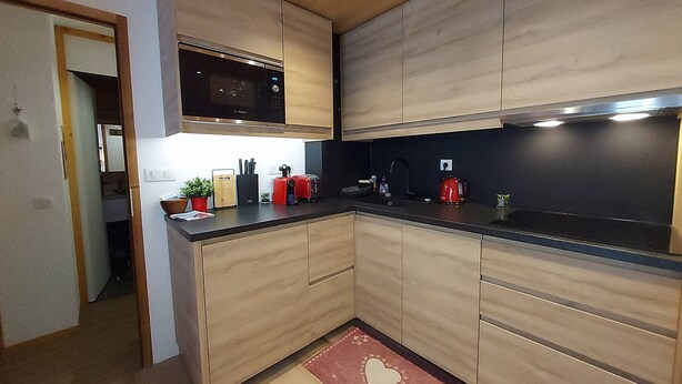 A modern kitchen with wooden cabinets, a black countertop, a microwave, a toaster, and a coffee maker. - 2-room apartment in Valmorel, near slopes and shops, equipped, wifi, non-smoking (Valmorel)