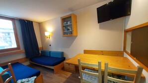 A compact room with a wooden table, blue sofa, and a TV mounted on the wall.