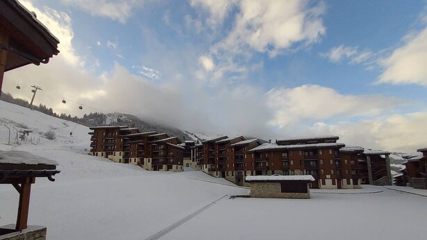 A snow-covered ski resort with multi-story buildings, ski lifts, and a clear sky.