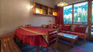 Una habitación acogedora con una mesa de madera y bancos, un sofá y una ventana con vistas a árboles.