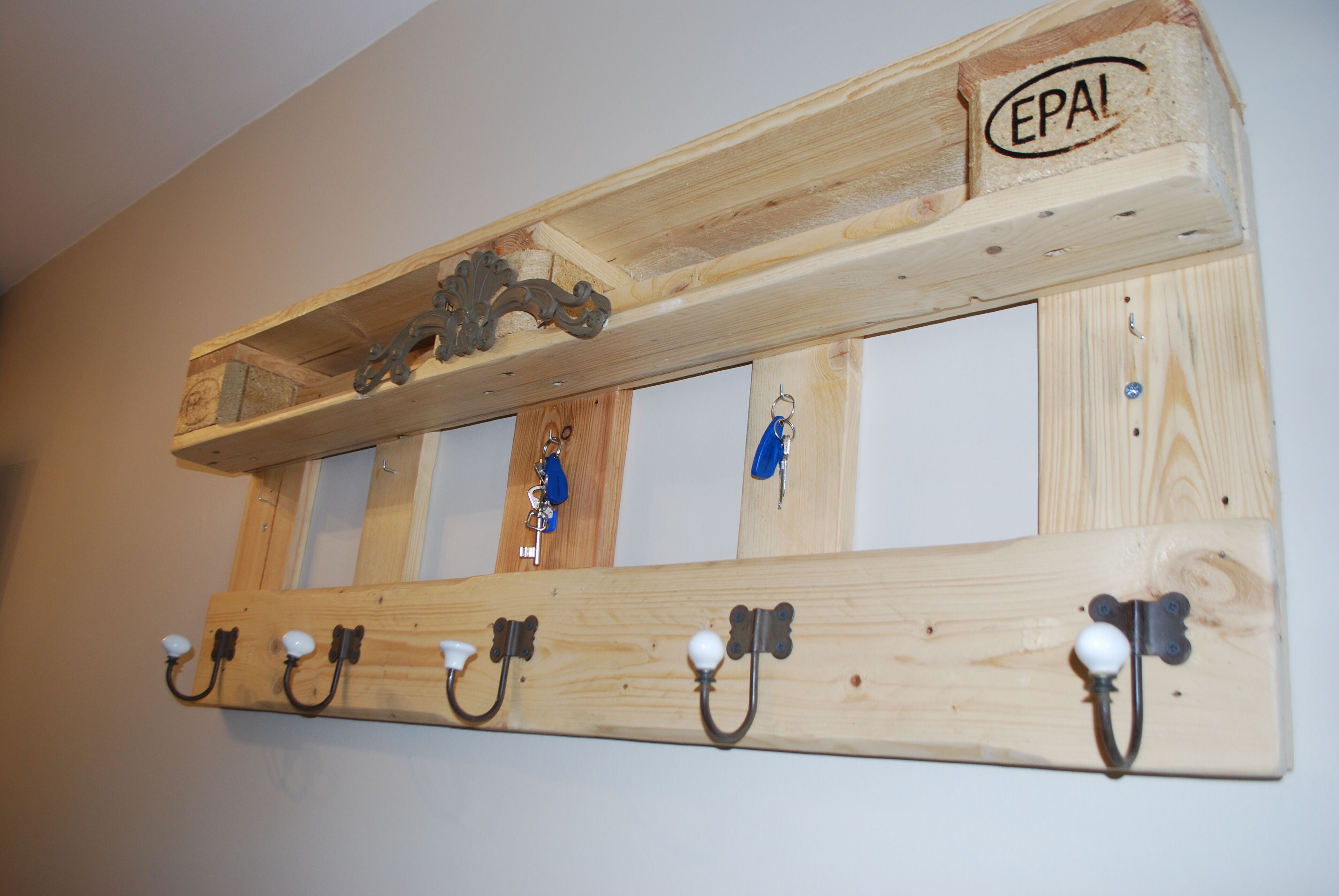 Un perchero de madera con ganchos y una pieza decorativa en la parte superior que dice "EPAI".