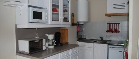 Et kompakt køkken med hvide skabe, en mikrobølgeovn, kaffemaskine og opvaskemaskine.