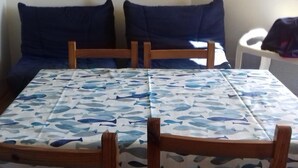Et værelse med et bord dækket af en borddug med fiskemønster, to blå polstrede stole, en hængende quilt med stjernemønster og et vindue med udsigt.