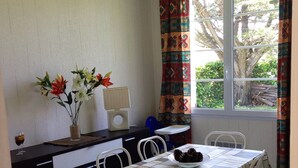 Een eethoek met een tafel voor vier personen, witte stoelen, een bloemenvaas en een raam met gordijnen.