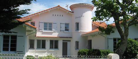 A two-story building with a white facade, a red-tiled roof, and a central tower.