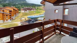 A wooden balcony overlooking a ski resort with multiple buildings, a ski lift, and a mountainous backdrop. - Divisible studio + mezzanine, ski-in/ski-out, sleeps 5, Valmorel (Valmorel)