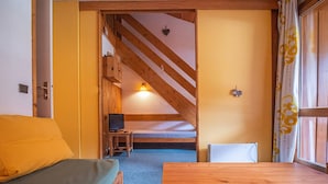 A cozy room with a wooden table, a bed with a green mattress, and a small TV on a wooden stand. - Divisible studio + mezzanine, ski-in/ski-out, sleeps 5, Valmorel (Valmorel)