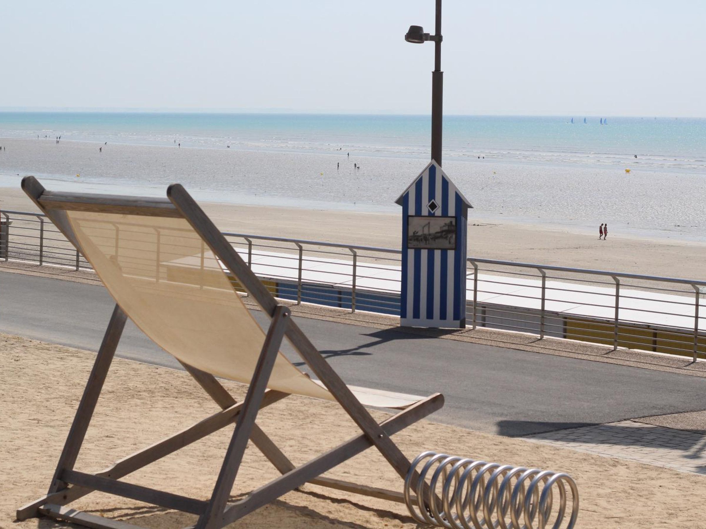 A beach with a metal railing, a beach chair, and a small blue and white structure.