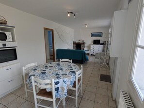 A room with a dining table, chairs, a bed with a green cover, a TV, and a white cabinet.