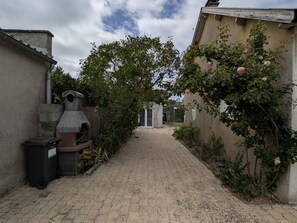 A narrow paved pathway leading to a building with a chimney and a trash bin on the left. - Charming single-storey house in St-Pair-sur-Mer, near the beach (Saint-Pair-sur-Mer)
