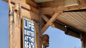A wooden beachside structure with a sign stating "LIFE IS BETTER AT THE BEACH" and another sign below it that reads "SURF NOTHING ELSE MATTERS."