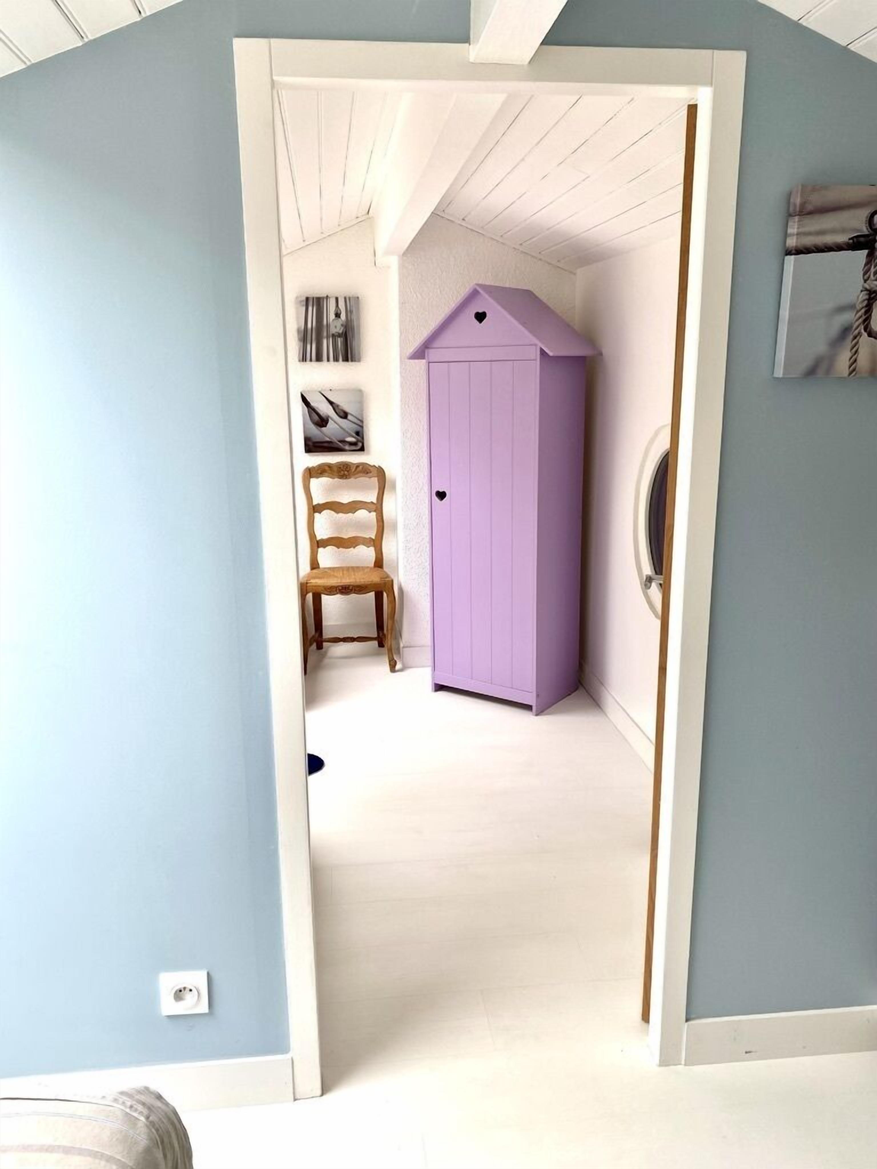 Un couloir avec une armoire violette, une chaise en bois et une porte blanche.