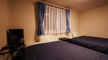 Une chambre d’hôtel avec deux lits, un téléviseur posé sur un meuble et une fenêtre avec des rideaux.