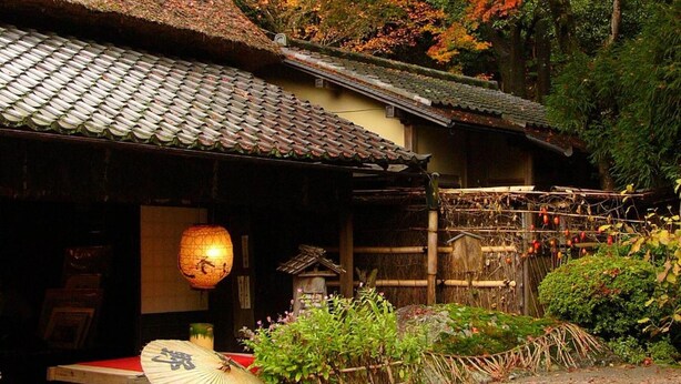 Een traditioneel Japans gebouw met een pannendak, omgeven door herfstbladeren.
