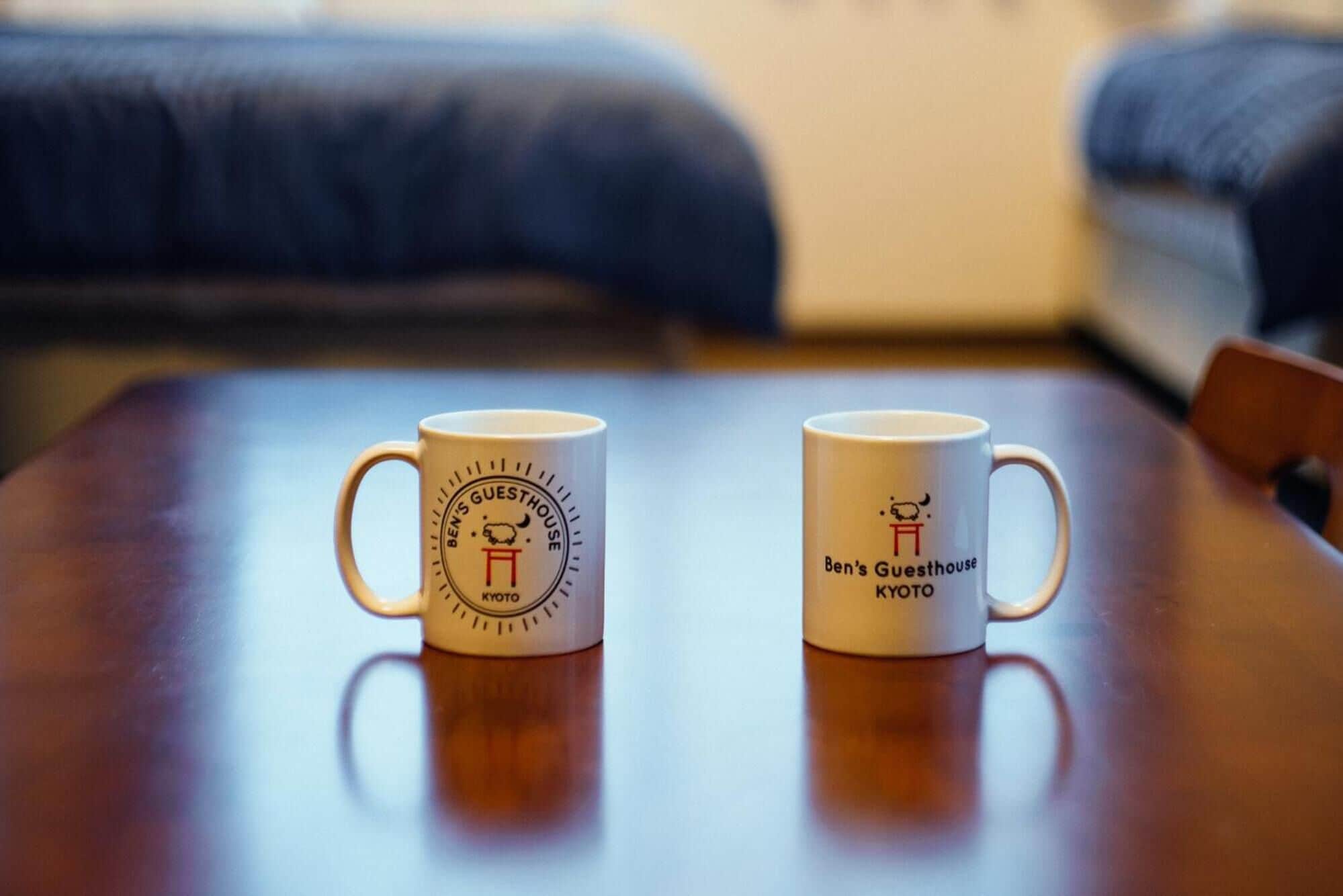 Two white mugs with logos on a wooden table.