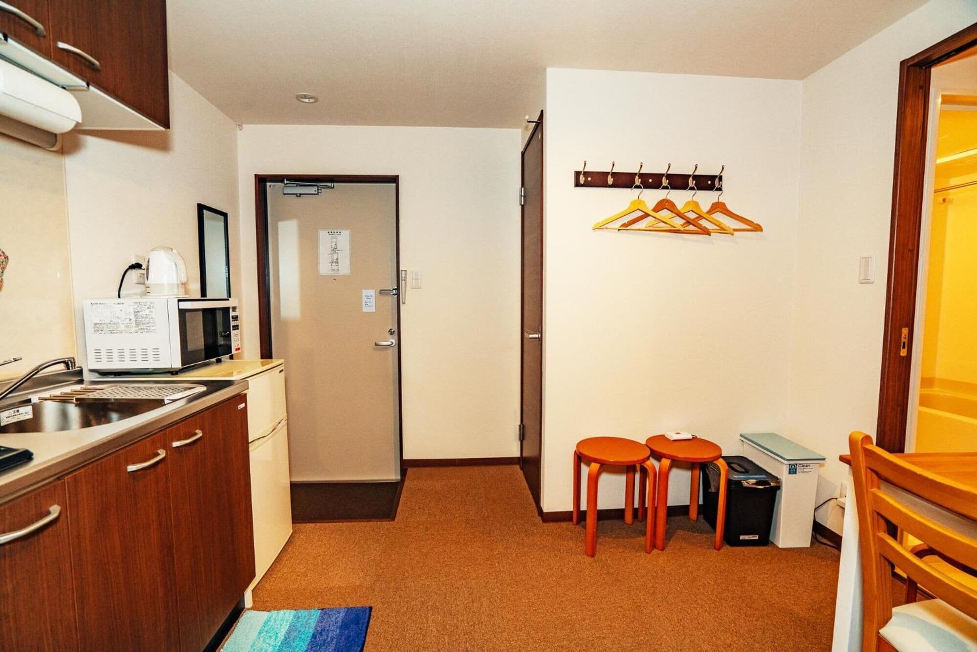 Una habitación de hotel compacta con kitchenette, un pequeño comedor y una puerta que da a un baño.