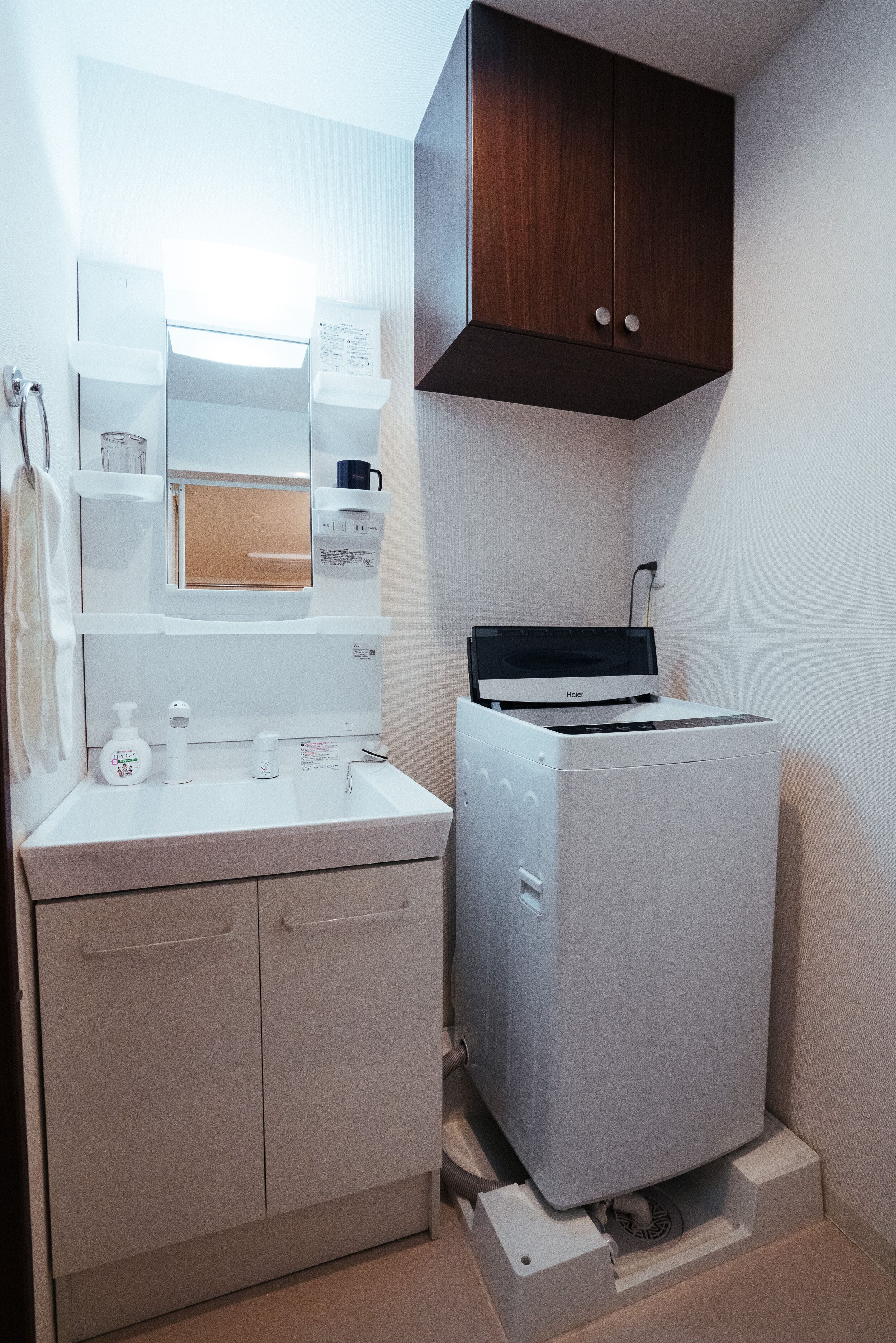A compact laundry room with a white washing machine, a sink, and a cabinet with a mirror above it.