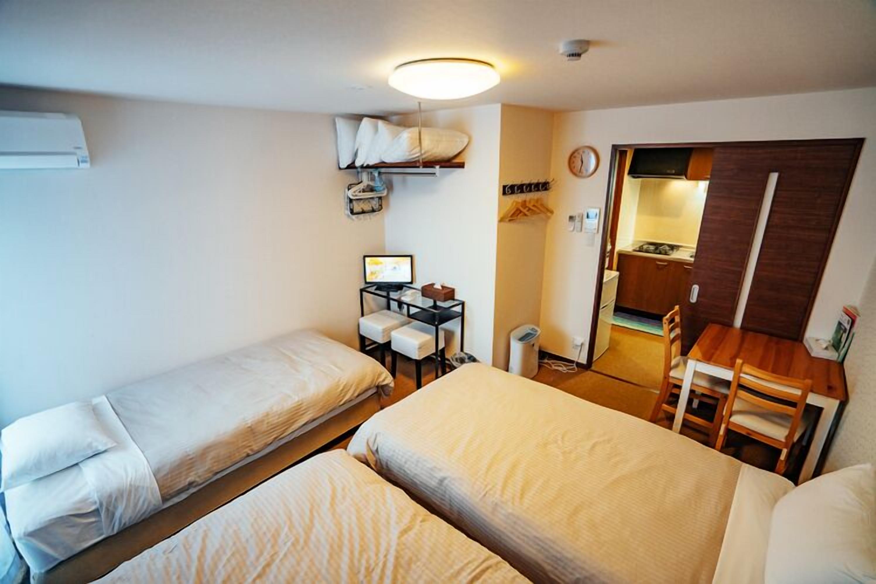 Une chambre d’hôtel compacte comprenant deux lits simples, un petit bureau avec un ordinateur, une chaise et une kitchenette.