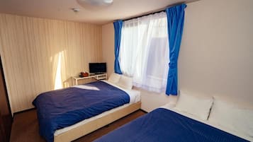 A hotel room with two beds, a television on a side table, and a window with blue curtains.