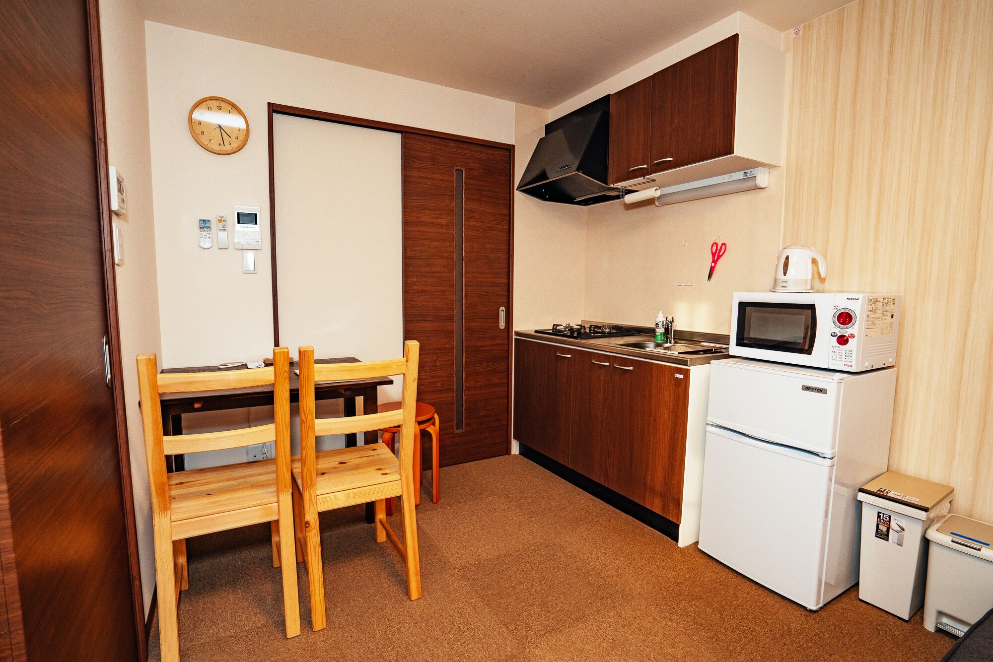 A compact kitchen with wooden cabinets, a microwave, a stove, and a small refrigerator.