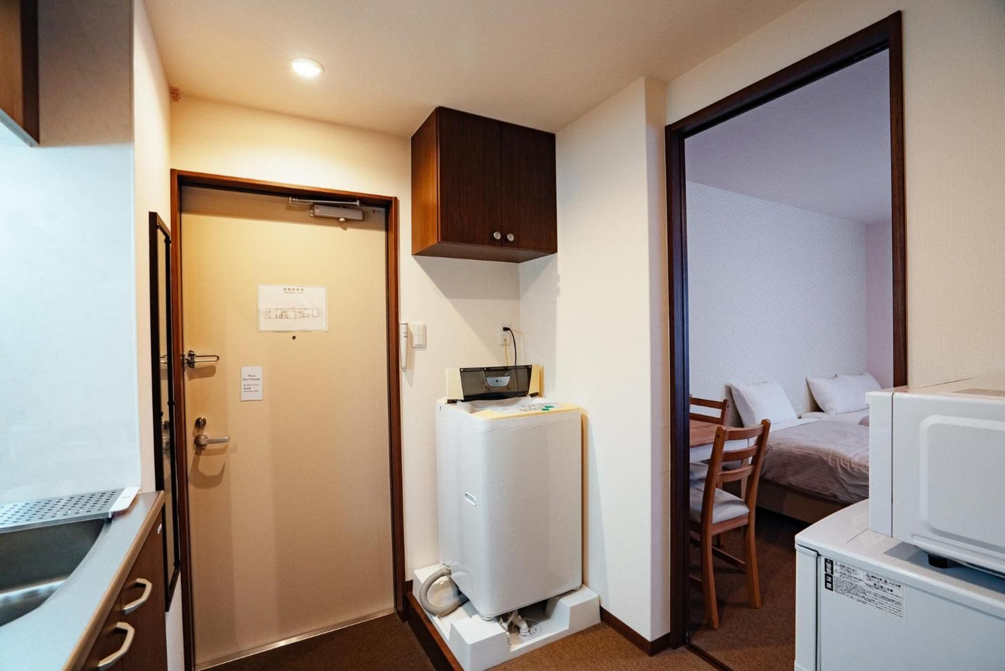 Una habitación de hotel compacta con kitchenette, cama, escritorio y baño pequeño.