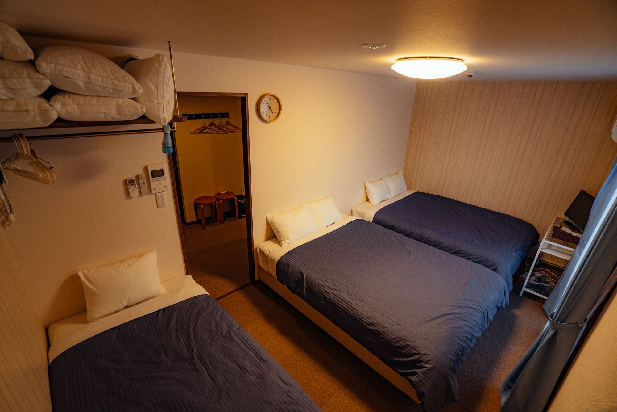 A hotel room with two beds, a mirror, a clock, and a coat rack with hanging items.
