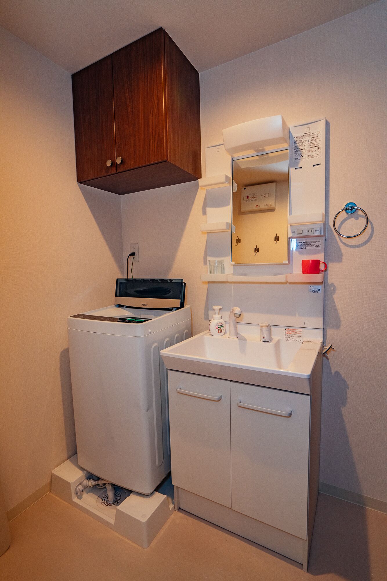 A compact laundry room with a front-loading washer and dryer, a small sink with a soap dispenser, and a wooden cabinet above.