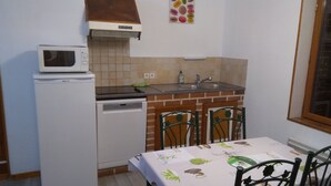 Cucina compatta con frigorifero, microonde ed elettrodomestici. Presente un lavello con rubinetto, una finestra e un tavolo con sedie.