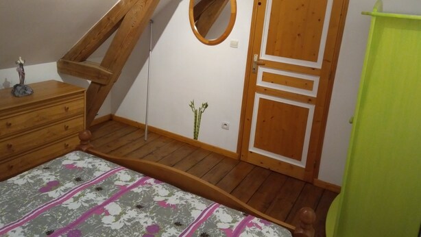 Una camera da letto con soffitto spiovente, pareti in legno, un letto con copripiumino floreale, una cassettiera, un armadio verde e una porta con uno specchio circolare.
