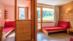 A cozy cabin with a wooden interior, a loft bed, a bench, and a window with curtains.