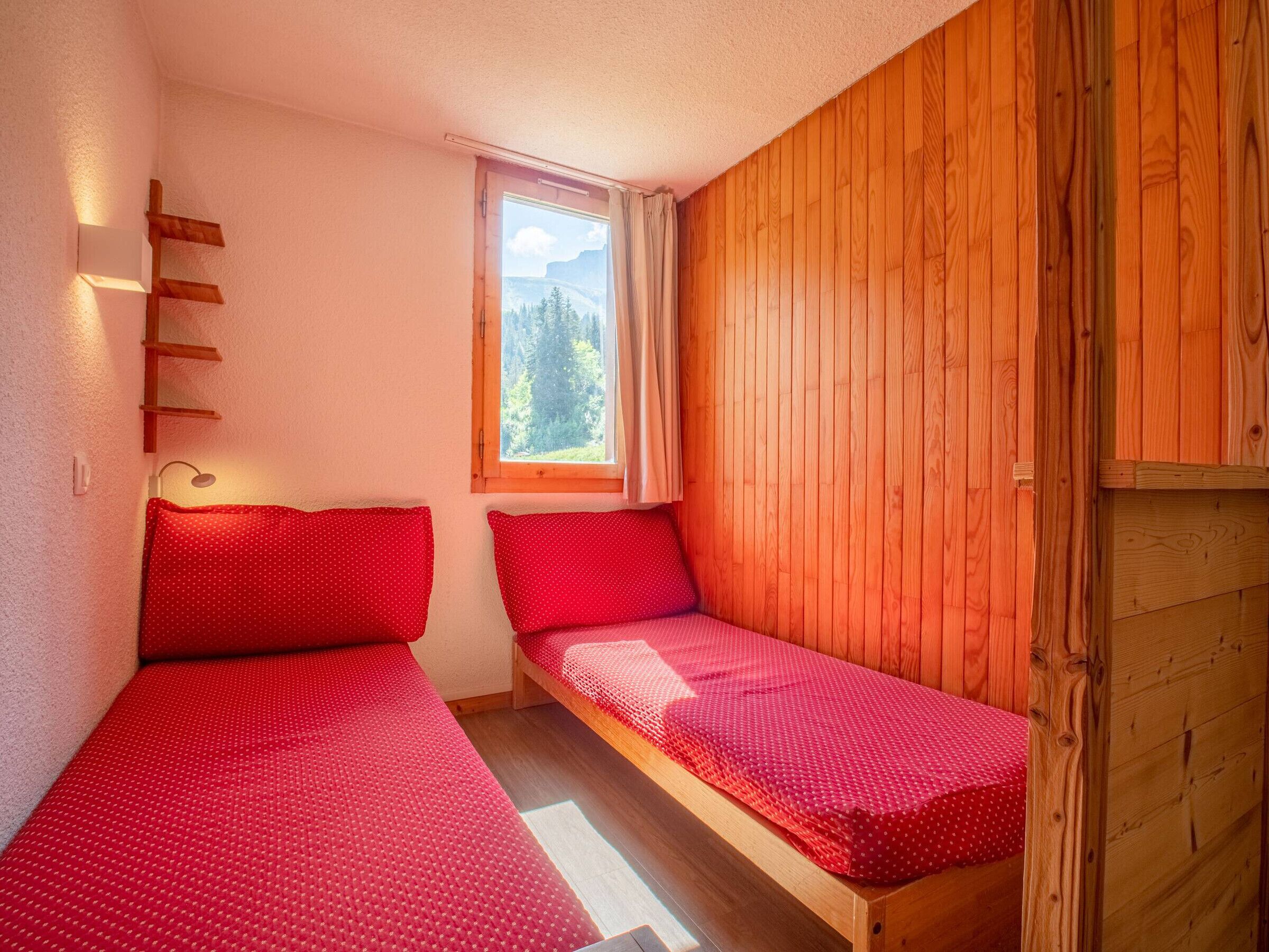 A small, cozy room with two single beds, a window with a view of a forest, and wooden walls.